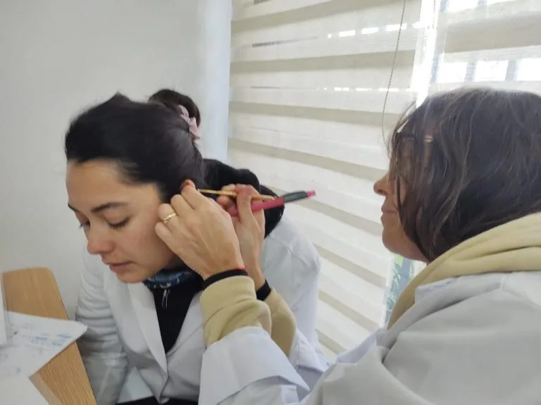 Tutora localizando puntos auriculares con un instrumento de presión en la oreja de una alumna.